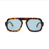 A pair of oversized square sunglasses with a dark brown and amber tortoiseshell frame and light blue lenses, shown against a plain white background.